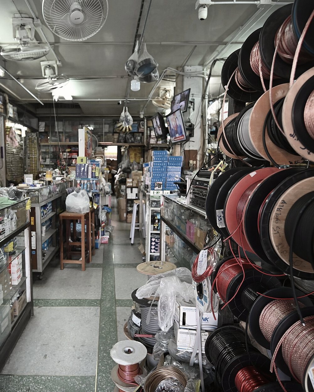 A narrow supply-shop aisle lined with wire spools and parts bins.